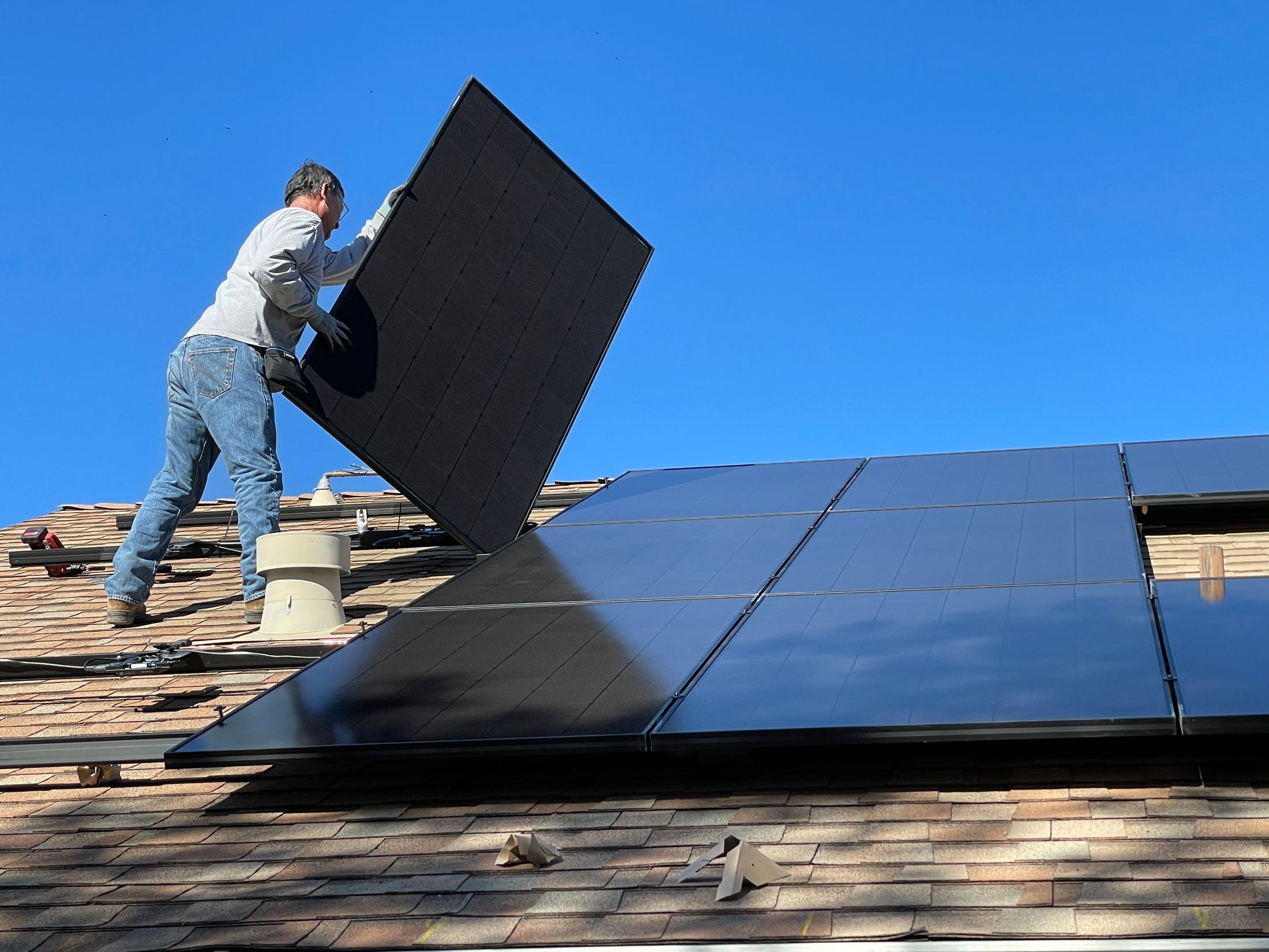 Installateur posant un module photovoltaïque noir sur une toiture, ciel bleu profond