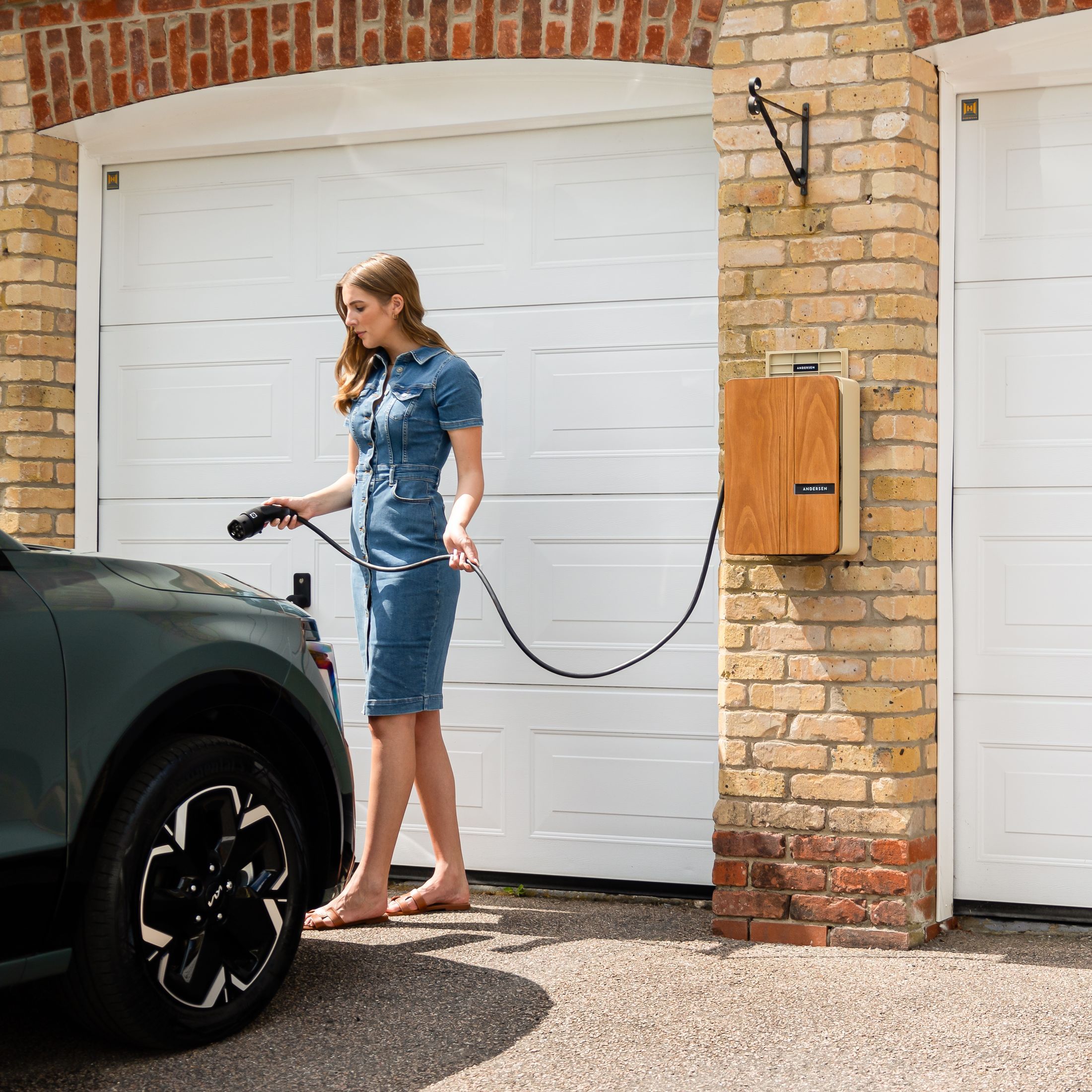 Personne branchant une voiture électrique sombre à une borne murale devant une porte de garage