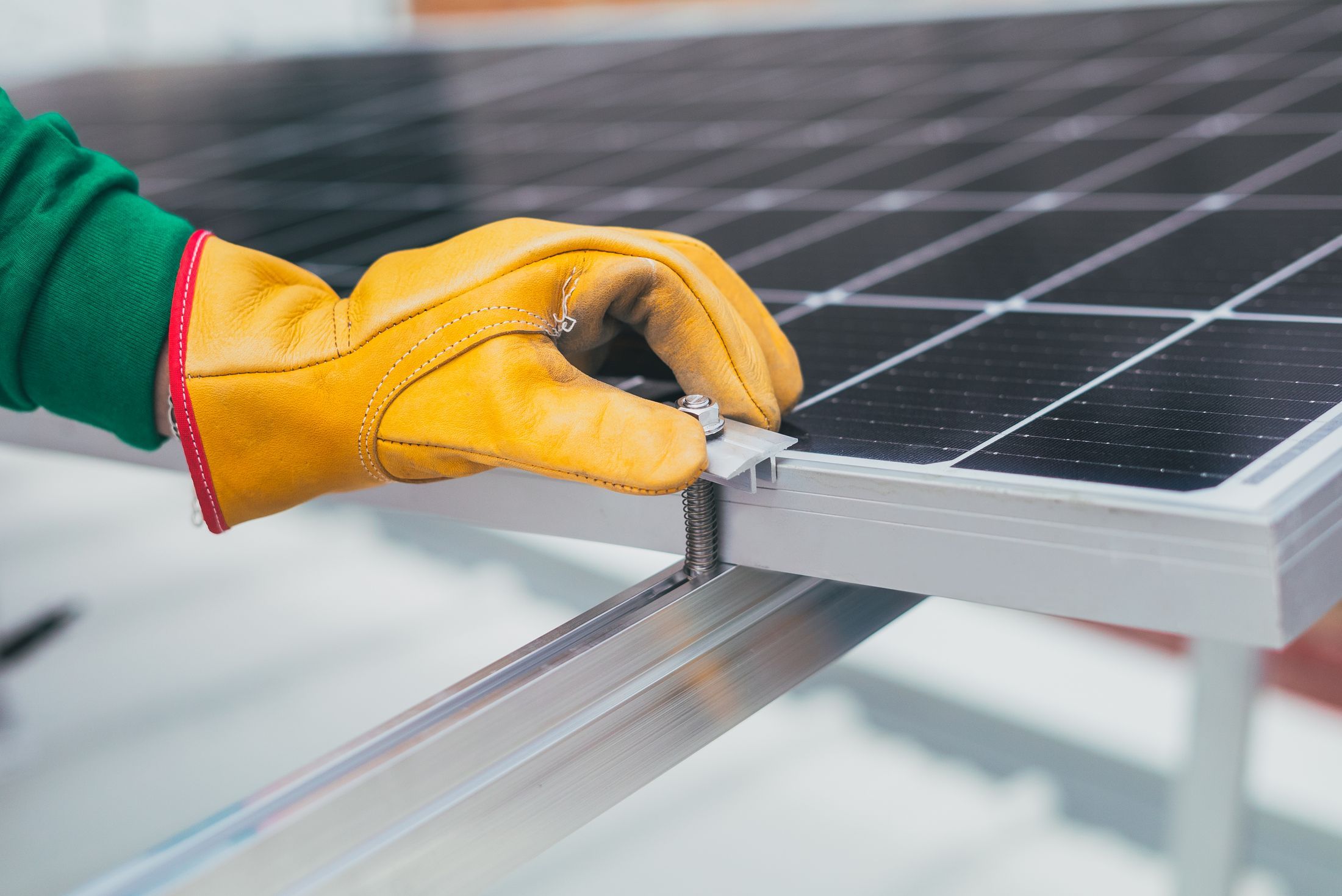 Main gantée serrant une fixation sur un rail sous un module photovoltaïque