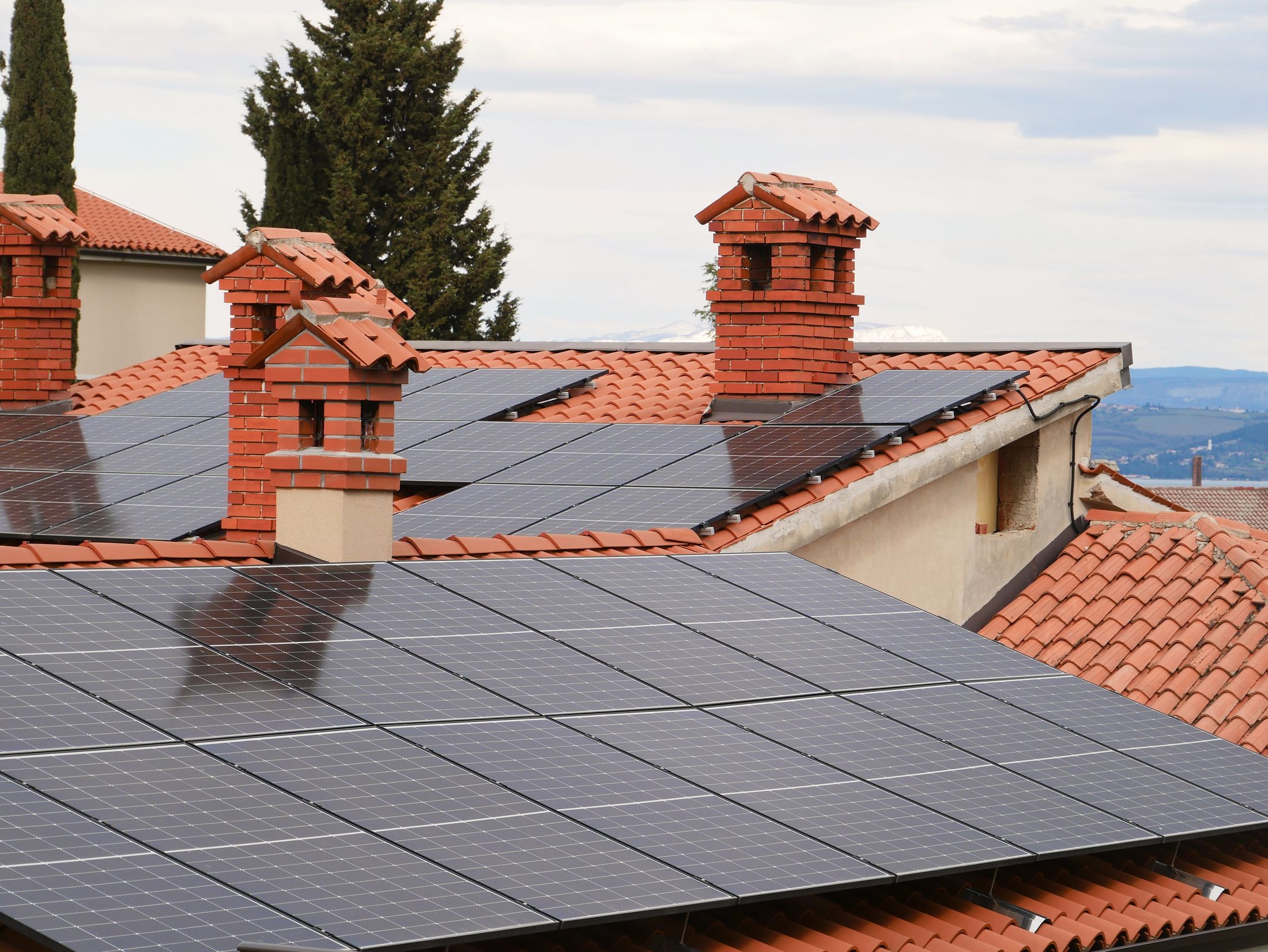 Toits en tuiles couverts de modules photovoltaïques, cheminées et ciel clair