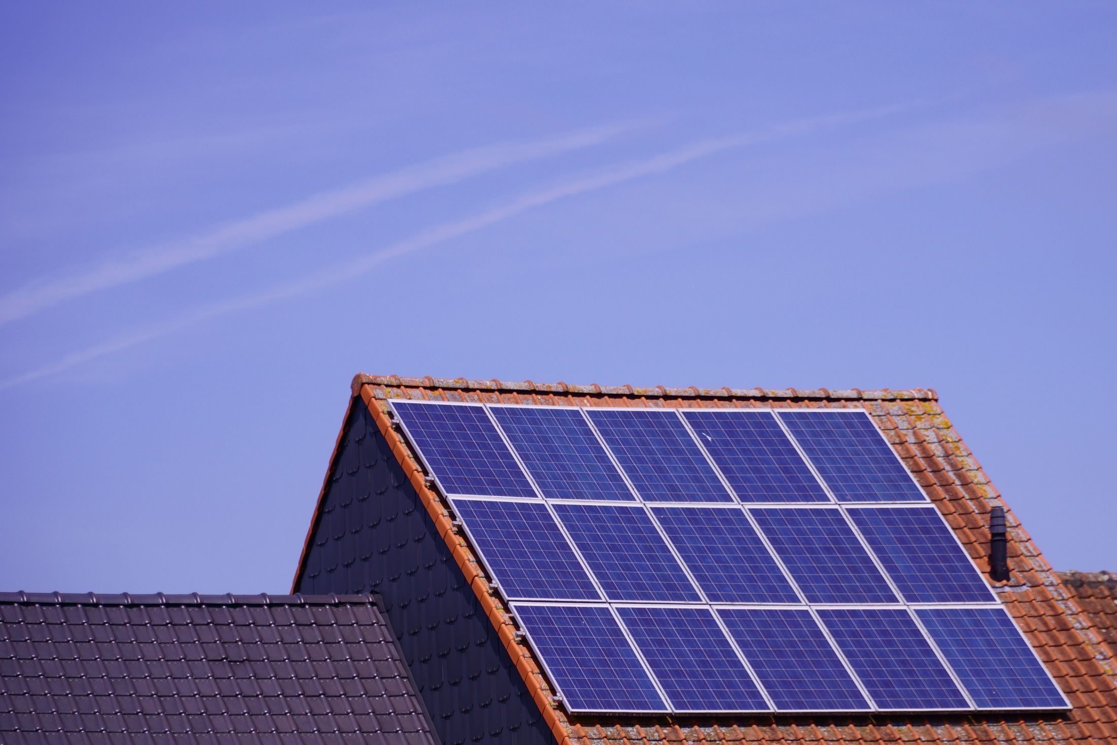 Modules photovoltaïques sur un pan de toiture en tuiles rouges, ciel bleu